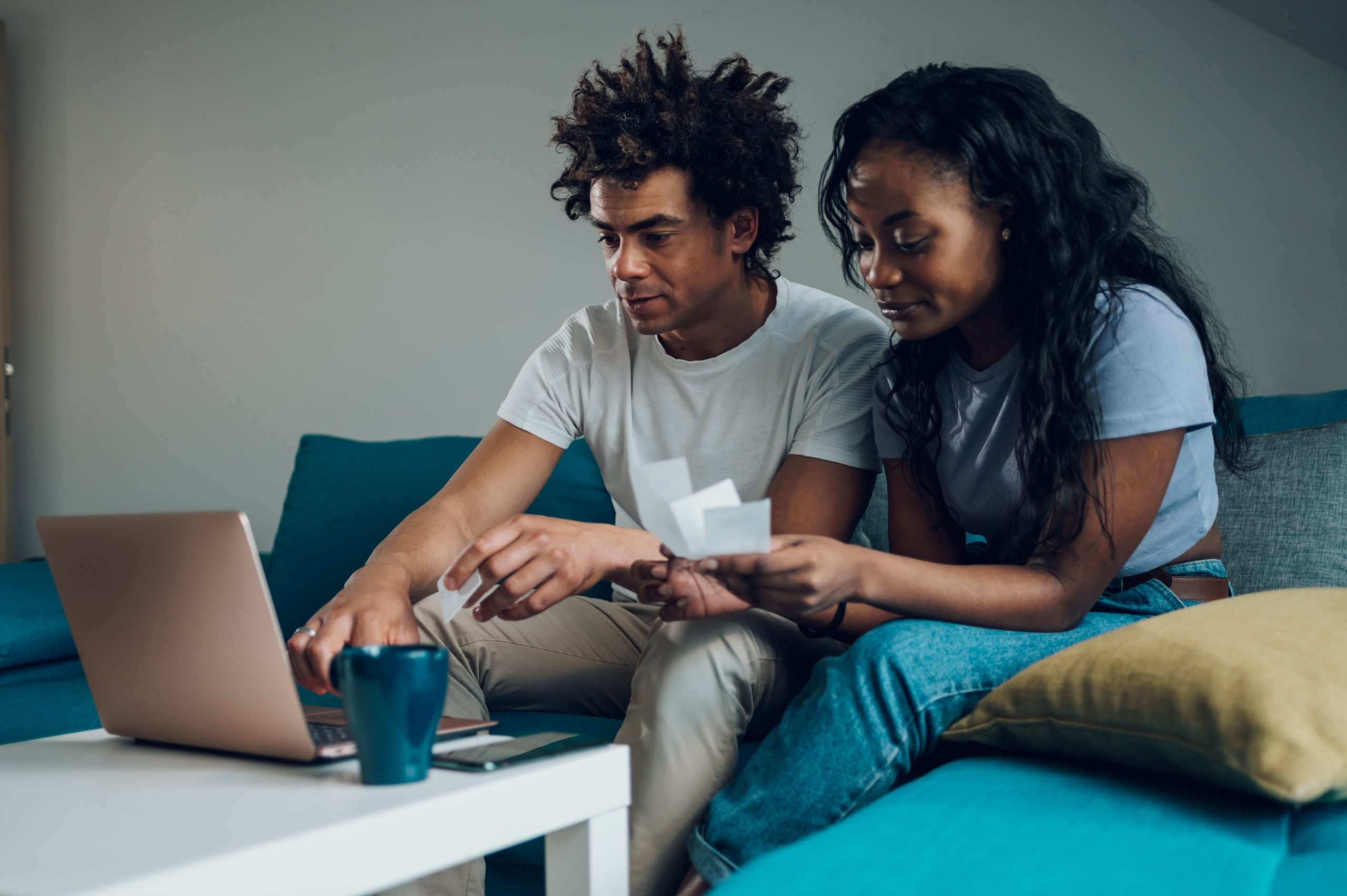 African american family couple sitting at home with a laptop and a credit card and paying monthly bills or online shopping. Using online banking application, reviewing taxes, domestic bills.